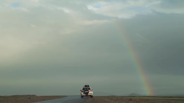 Carro branco dirige em uma estrada sob um arco-íris brilhante — Vídeo de Stock