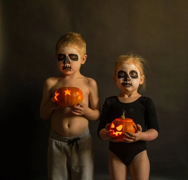Çocuklar, ellerinde balkabağı olan bir kız ve bir oğlan. Cadılar Bayramı 'nda karanlık arka plandaki kameraya bakın.
