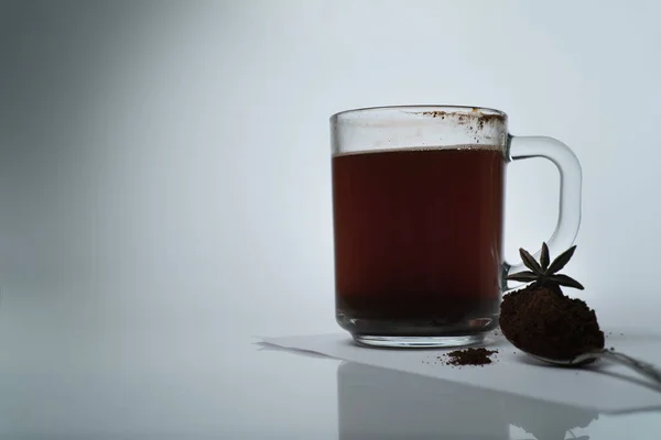 Xícara transparente com café natural e uma colher de café moído com anis estrelado em um fundo claro — Fotografia de Stock