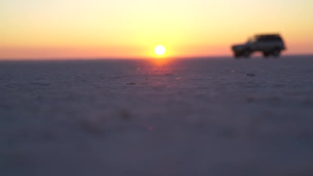 Автомобіль їде на плоскій піщаній поверхні на тлі світанку — стокове відео