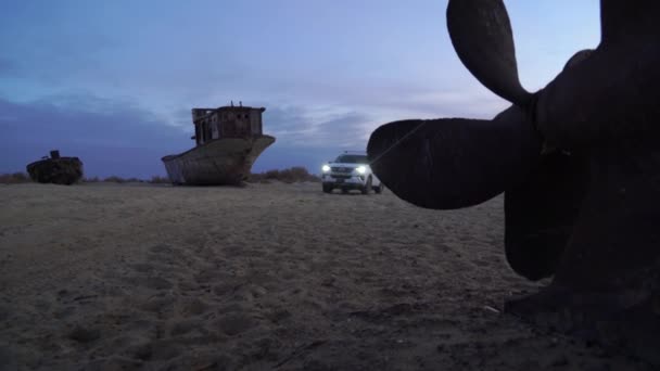 Муйнак Узбекистан, 25 декабря 2019 года: автомобиль проезжает мимо заброшенных судов в сухом море — стоковое видео