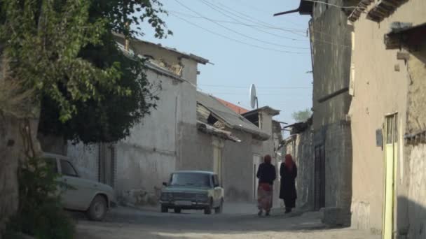 Samarkand-usbekistan 09.09.2019 enge Oststraße, auf der zwei Frauen in orientalischer Kleidung spazieren gehen und ein Auto vorbeifährt — Stockvideo