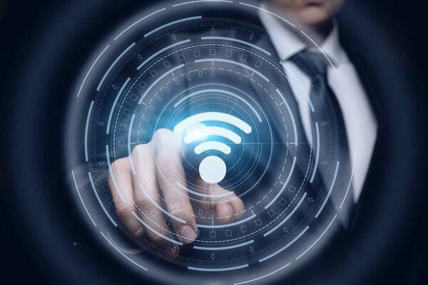 Businessman clicks on the symbol of the free WiFi on dark background.