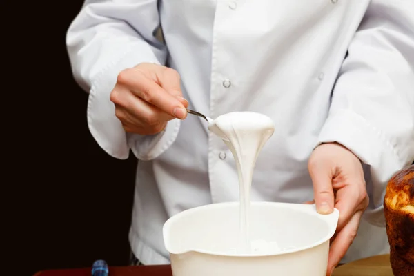 A cooker is beating foamy white cream in a bowl with a spoon for a cake. Preparation cream.
