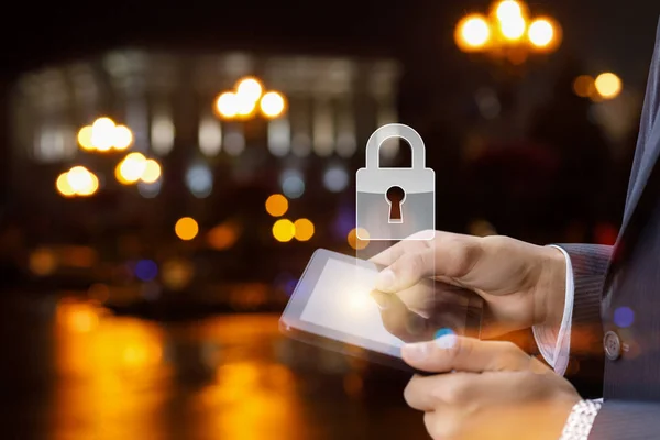 The concept is the mobile devices protection system. A padlock is hanging above the device in the hands of a businessman at the night city centre background .