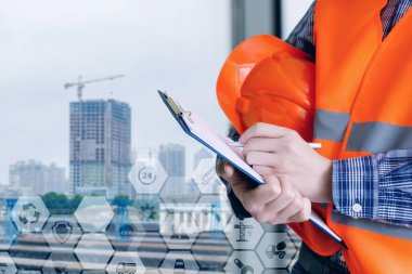 Üniformalı bir Oluşturucu inşaat zemin ve sembolleri arka plan içinde bina ile tarak notlara yapıyor.