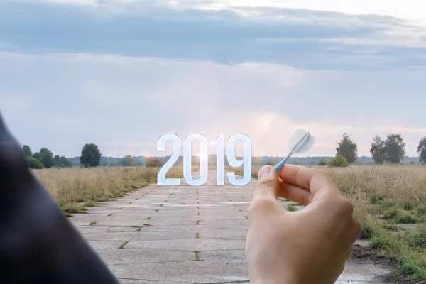 A man with a dart in his hand is standing opposite the numbers of coming year at the wide road background. The concept is the opportunities and perspective of coming year