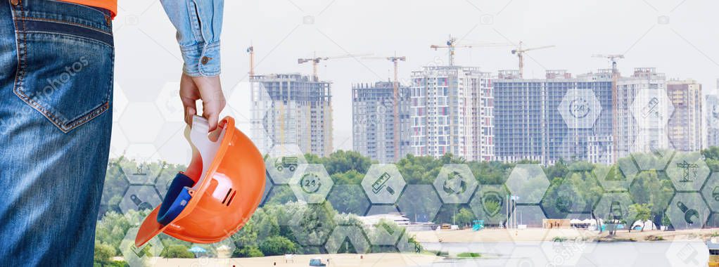 An engineer with a building helmet in his hand is standing opposite the set of city skyscrapers. The concept is the development of urban life.