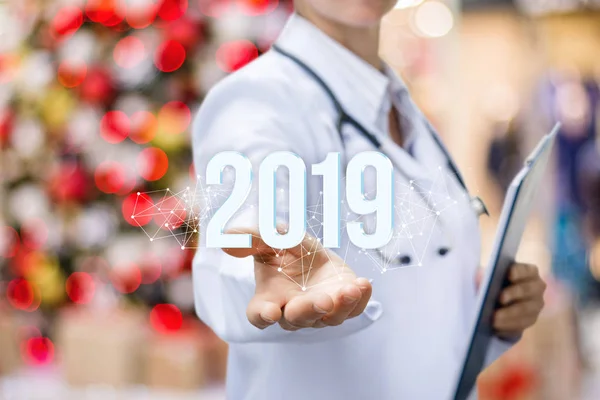 A doctor with a stethoscope is showing the numbers of coming year in her hand at the bright lights background. The concept is the future development of medical service.