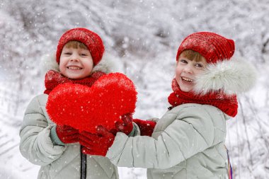 İki küçük mutlu gülen kız ikiz benzer parlak giysiler içinde büyük konforlu kırmızı kalp onların elinde tutuyor. Sevgililer 's gününde olumlu duygular bir kavramdır