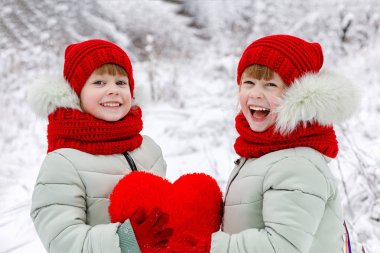 Kız kardeş ikizler gülüyor giyinmiş olarak parlak kıyafetleri, büyük kırmızı bir kalp kış park arka plan, ellerinde tutan içtenlikle gülüyor. Sevgililer günü bir kavramdır