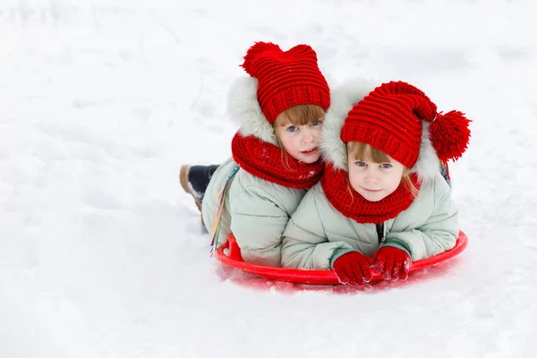 有趣的姐妹双胞胎躺在塑料盘子上 享受着在冬日公园雪山上的雪橇 这个概念是孩子们在冬天玩耍 — 图库照片