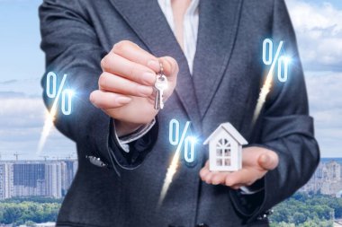 Bir iş kadını kıyafetli bir anahtar ve bir ev modeli avucunun büyük şehir panorama arka plan, ön plan ayakta yüzde simgeleri ile üzerinde tutuyor. Mali mortgage prensip bir kavramdır.