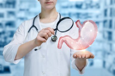 Boynunda steteskop ile genç bir doktor ayakta ve eline bir büyüteç bulanık laboratorian Oda arka plan, yukarıda asılı mide modeli bakarak.