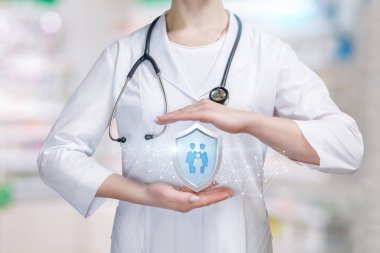 Genç bir doktor grubu simgesinin kişi veya aile üyeleri içinde koruyucu jest olarak onun avuç içi arasında büyük bir kalkan tutuyor. Aile Hekimliği ve hayat ve sağlık sigortası kavramı.
