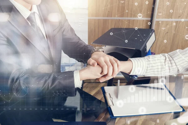 A closeup of businessman and his partner shaking hands above the table covered with papers in office with growth diagram image and network structure on foreground. The successful agreement concept.