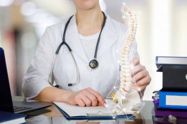 Pelvis parçası ile bir spin iskelet tutan masada bir doktor.
