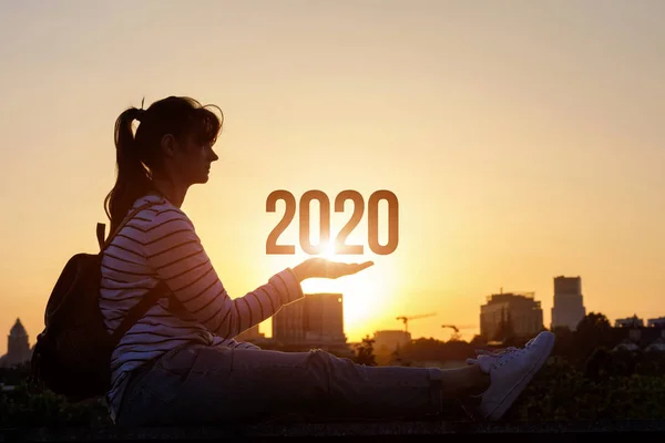 The woman shows the figures for 2020 background urban sunset.