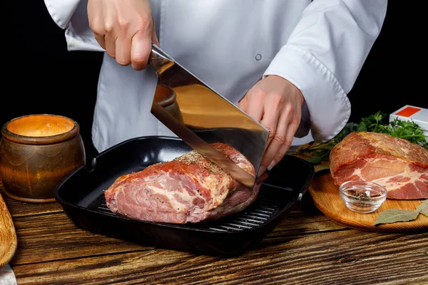 The cook cuts the ham, using a hatchet . — Stock Photo, Image