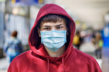 Bir tren istasyonunun bulanık arka planında maske takan genç bir adam var..