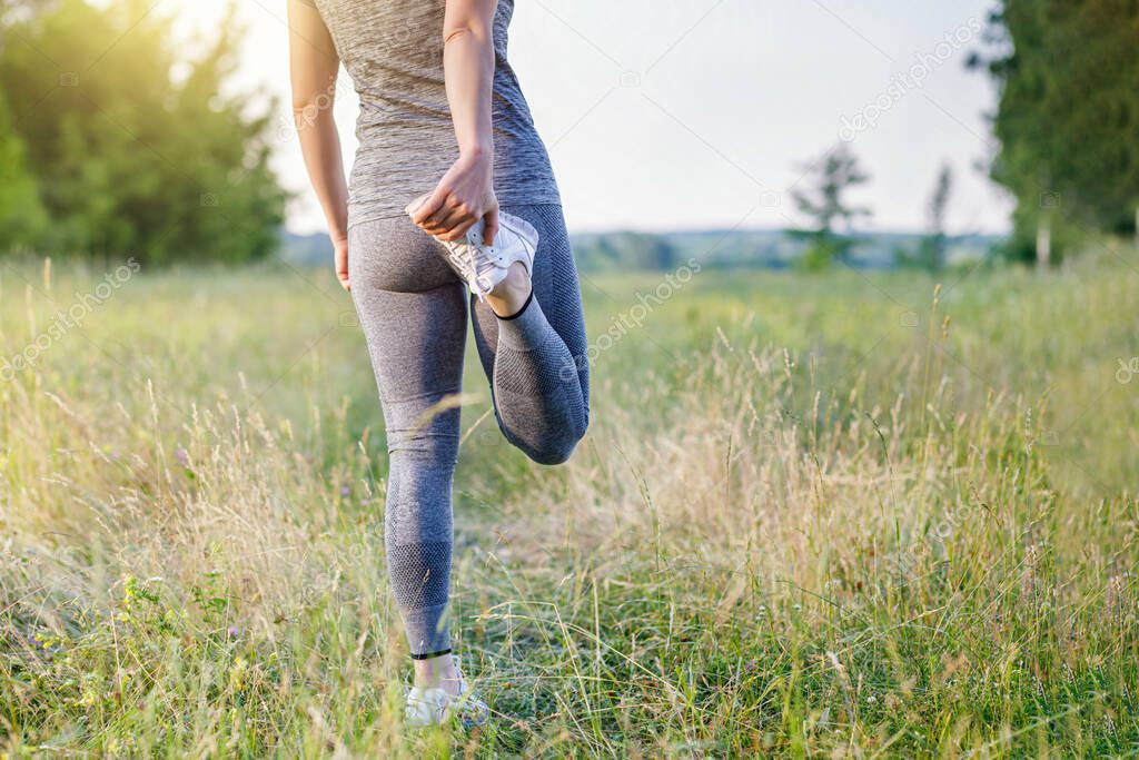 Woman stretches legs before jogging on nature background.