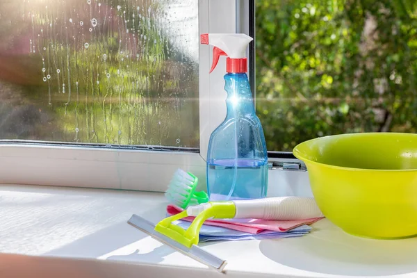 Window cleaning tools and cleaning agent are standing on the windowsill.