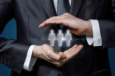 İşadamı el kol hareketi yaparak mavi arka plandaki işçilerin hologramlarını koruyor..