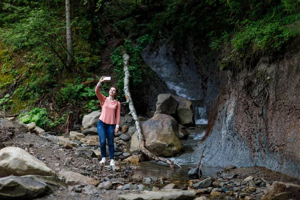 A woman photographs herself against the background of a waterfall.