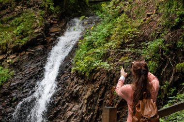 Bir kadın sırtında sırt çantasıyla telefonda bir şelale alır..