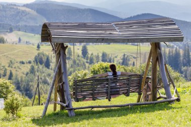 Bir kadın salıncakta oturmuş dağlara bakıyor..