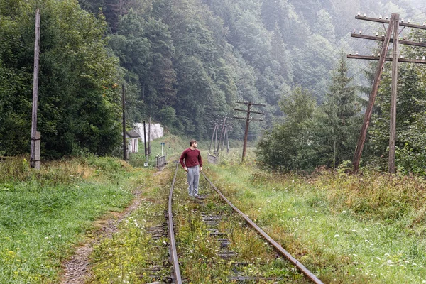 一个年轻人站在山林的铁轨上 — 图库照片