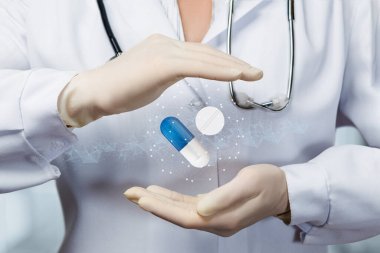 Doktor bulanık bir arka planda koruyucu bir jest ile ilaç hapını korur..