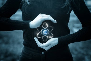 Yaratıcı eller içinde toprak olan parlayan atom sembolünü tutarlar. Bir insan, merkezinde Dünya 'nın olduğu ve bilim ve özeni vurgulayan ışıldayan bir atom sembolünü nazikçe kucaklar..