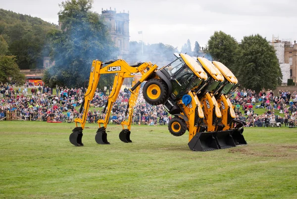 Üç sarı Jcb kazıcı yükleyici ve Chatsworth ülke adil bir gösterisinde performans dans Diggers, onların backhoes dinlenme başlıklı ve kova ile jant yüksek havada, hazır Araçlar altında geçmek için