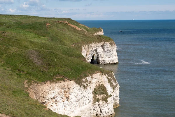 Güneşli bir günde çimlerle kaplı Flamborough Head 'deki beyaz tebeşirli uçurumlar ve solunda kayalıklar.