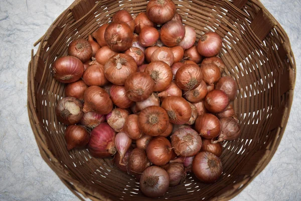 Top view of small onions stored in round brown wicker bamboo basket in Indian and Pakistani household.