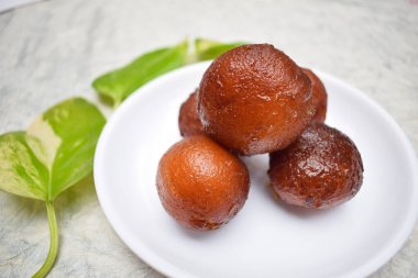 Gulab Jamun 'un beyaz arka planda beyaz tabakta tatlı Hint tatlısını yakın plan. Para fabrikası yapraklarıyla süslenmiş..