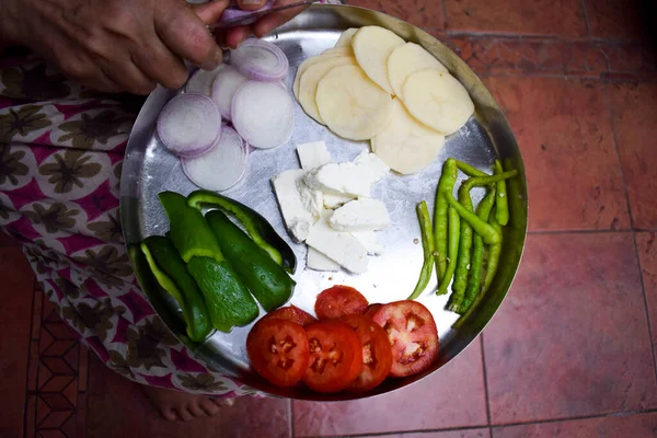 Indian woman chopping onions clices with a knife with both hands on Thali. Preparation for making Pakoda or curry sabji on thali. Traditional method of cutting vegetables in Indian kitchen