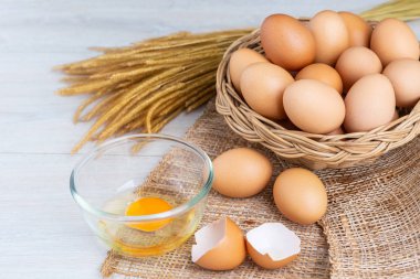 Bir ahşap sepeti ve sarısı beyaz ahşap bir masa üzerinde bir kasede yumurta.