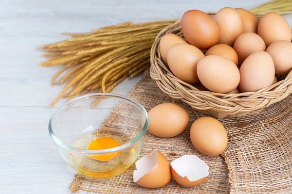 Bir ahşap sepeti ve sarısı beyaz ahşap bir masa üzerinde bir kasede yumurta.