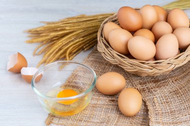 Bir ahşap sepeti ve sarısı beyaz ahşap bir masa üzerinde bir kasede yumurta.