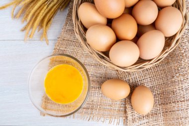 Bir ahşap sepeti ve sarısı beyaz ahşap bir masa üzerinde bir kasede yumurta.