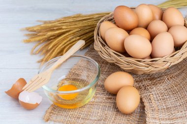 Bir ahşap sepeti ve sarısı beyaz ahşap bir masa üzerinde bir kasede yumurta.