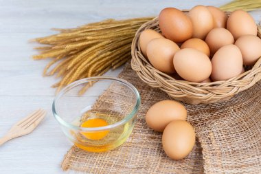 Bir ahşap sepeti ve sarısı beyaz ahşap bir masa üzerinde bir kasede yumurta.