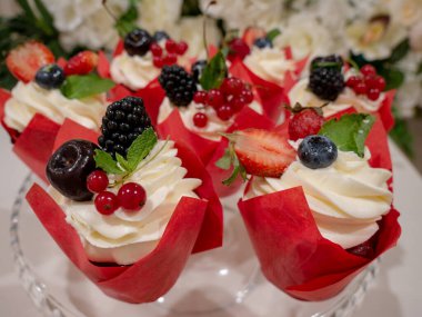 Kırmızı ambalaj kağıdına böğürtlen, meyve, krem şanti ve nane yapraklı lezzetli kekler. Yakın çekim, yumuşak odaklanma