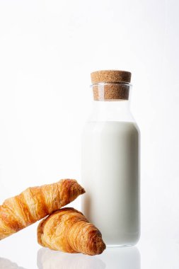 Beyaz arka planda süt lü şişe ve iki fransız kruvasan.