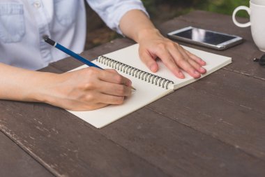 Defter fincan kahve ve telefon ile ahşap masa üzerinde yazma el kadın.