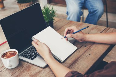 Not defteri yazma ve ahşap masa üzerinde dizüstü kullanarak genç iş adamı el.