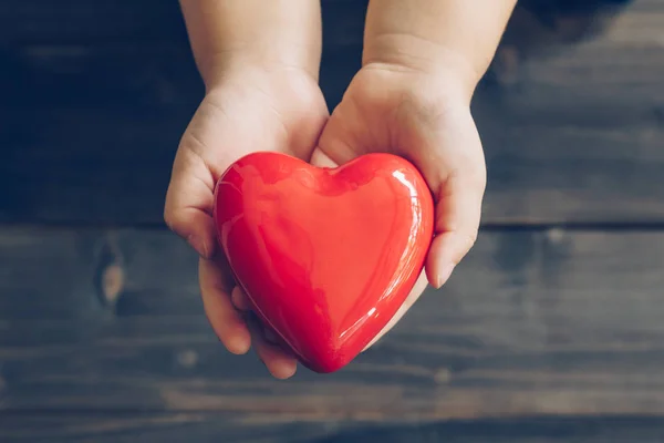 Close up children hands giving red heart on wood background