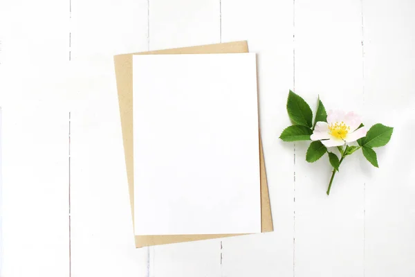 여성 결혼식 편지지, 꽃 바탕 화면 모형 장면 빈 인사말 카드, 크 래 프 트 봉투 및 피 야생 장미 지점. 오래 된 흰색 나무 테이블 배경입니다. 평면 위치, 최고 보기. — 스톡 사진
